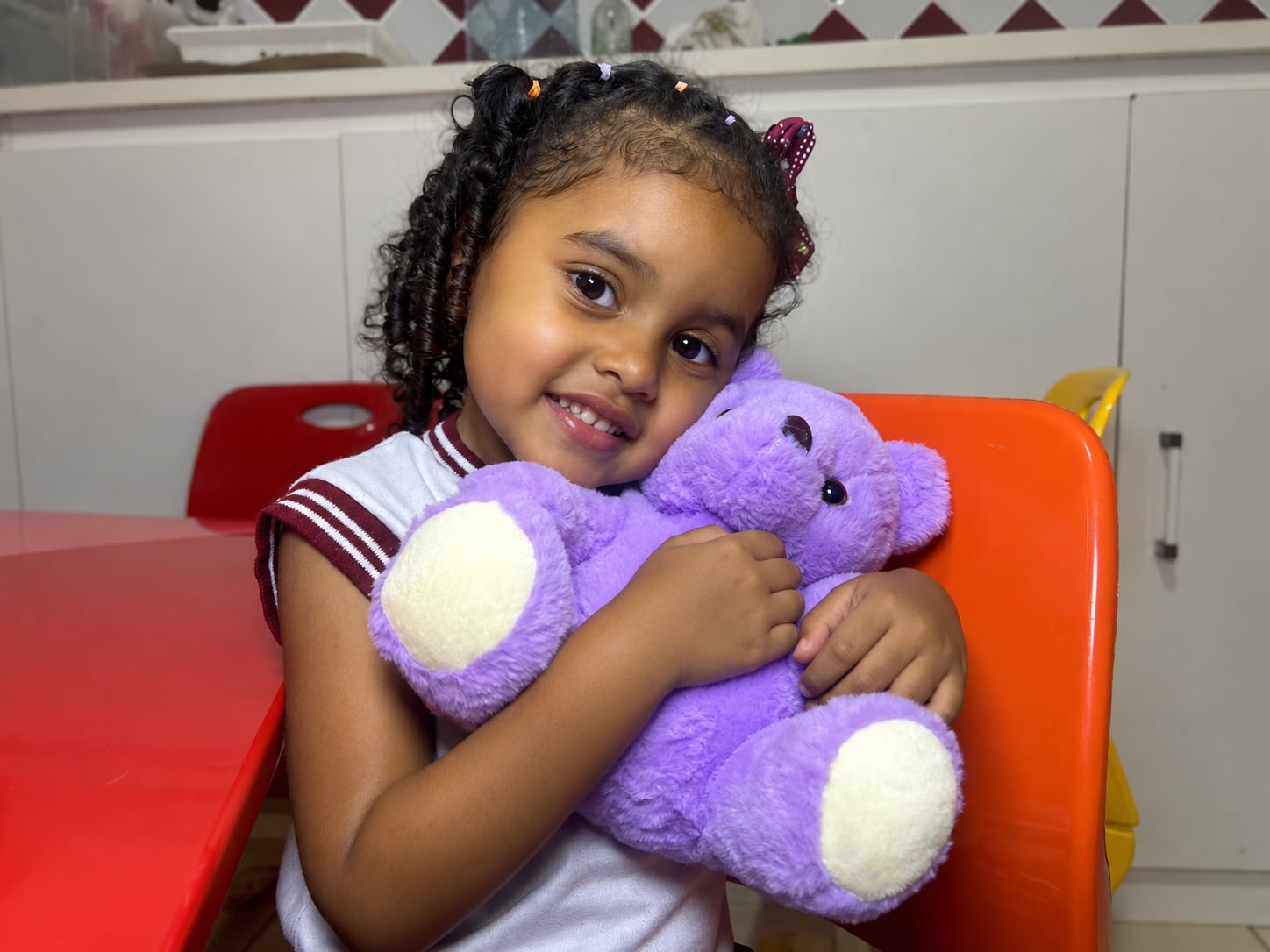 Aluna da Educação Infantil do CEC sorrindo e abraçando um ursinho de pelúcia lilás