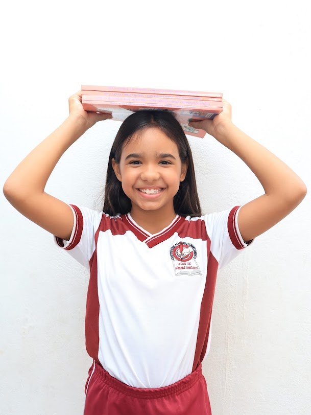 Aluna do Ensino Fundamental sorrindo com livros sobre a cabeça