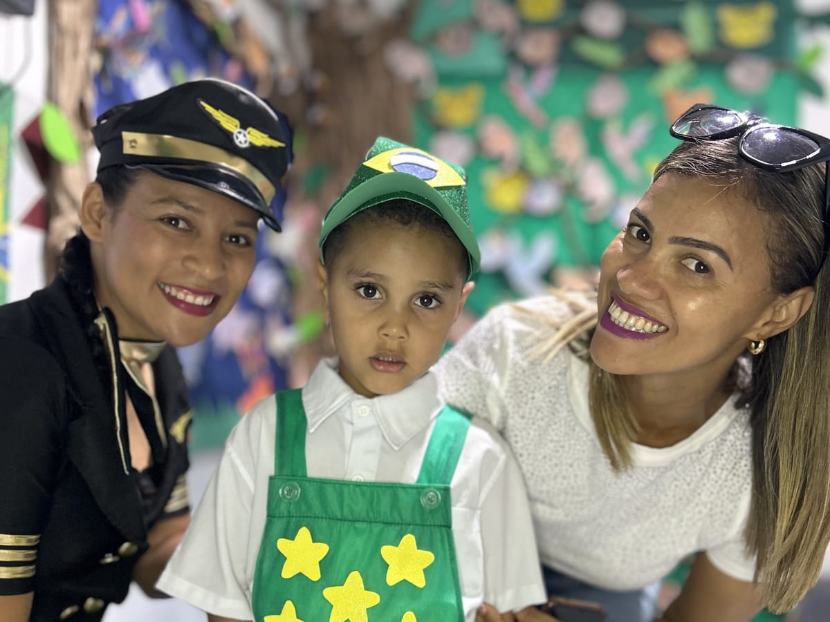 Aluno do CEC fantasiado, com a professora e a mãe, sorrindo juntos na escola